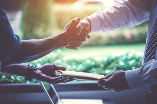 Two men shake hands as paperwork is exchanged between them.